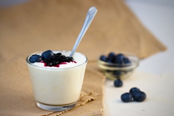 Glass cup of yogurt with blueberries on white table and white background