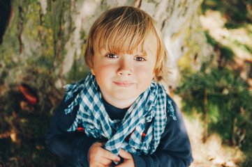 Outdoor close up portrait of sweet little toddler boy playing in the parc, wearing blue scarf