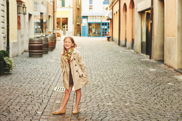 Outdoor fashion portrait of 8-9 year old hipster girl wearing stylish trench coat