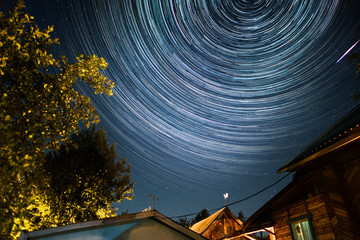 Starry sky with star trails over the wooden buildings - Powered by Adobe