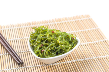 wakame seaweed salad in a ceramic bowl on bamboo mat. popular and delicious japanese food appetizer.