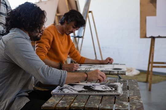 Male students painting on book at table