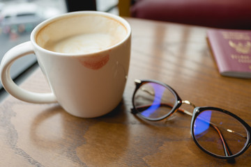 cup with coffee have lipstick kiss on the cup and have glasses placed beside on wood table in morning. image for beverage,food,accessory,fashion,business concept