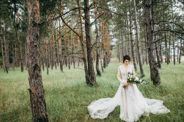 Beautiful, pretty bride with big bouquet in the forest