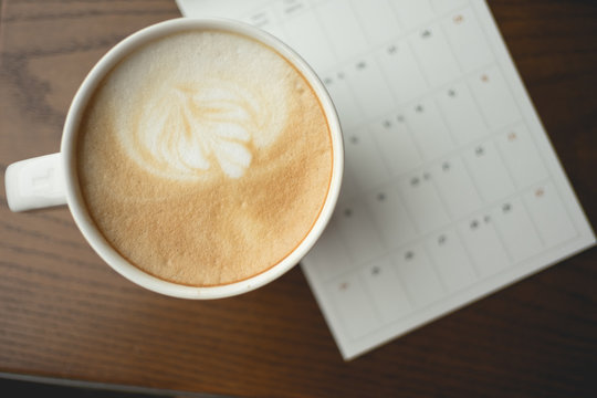 top view. cup with coffee placed beside calendar on wood table are background. this image for business,drink,beverage,food concept