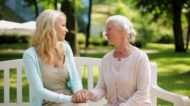 daughter with senior mother talking on park bench