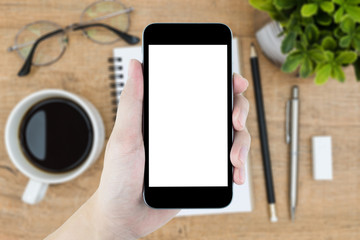 Hand holding smartphone with white blank screen over wood desk table.