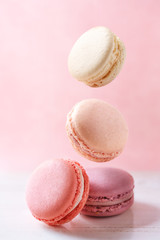 Colorful macarons on a pink background. French sweets falling from above on a white paper