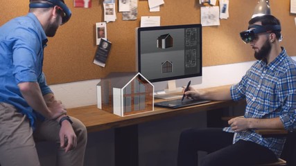 Young adult Caucasian colleagues architects using holographic augmented reality glasses together, discussing private house model hologram. 4K UHD RAW edited footage