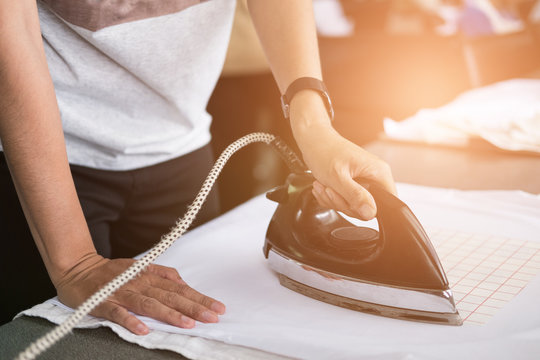 Young Woman Ironing Waterproof Film On Fabric At Shop. Worker Working On Manual Screen Printing On T-shirt.