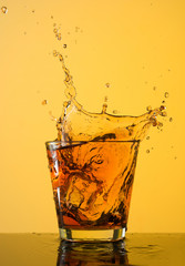 Whiskey splash out of glass on yellow background
