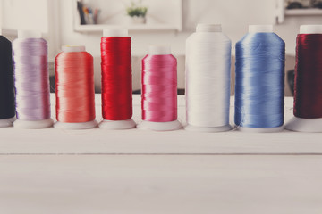 Colorful thread spools on wooden table close up