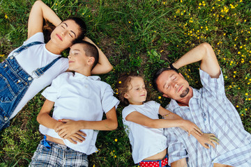 Fototapeta premium Happy family with two children closed eyes and lying on the grass. Top view.