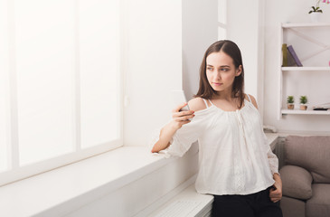Young thoughtful woman with smartphone at home