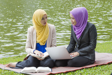 Two beautiful muslim women are discussing and changing idea while sitting down at park - 170461781