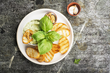 Appetizing crispy toasted grilled toasts with feta paste with walnuts, herbs, salt, garlic, fresh basil in ceramic ware on a gray stone background. Top view..