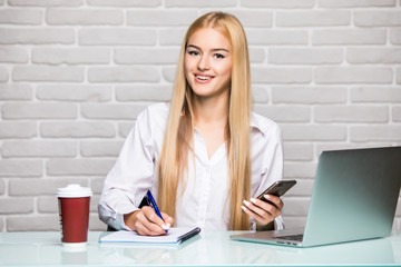 Portrait of a young business woman use phone and make notice in notebook at office