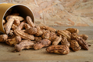 Raw peanuts in paper cans on wooden background
