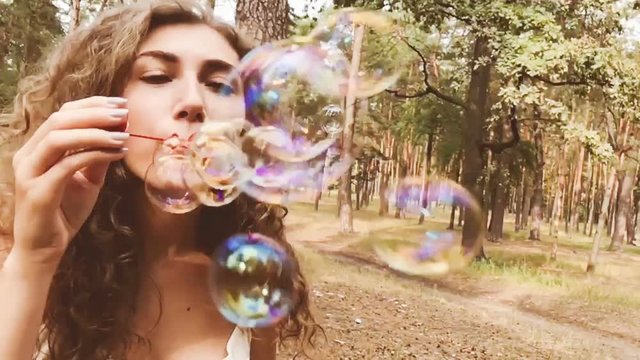 Attractive young woman blows soap bubbles in park in summer