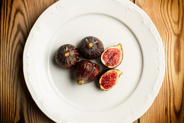 Plato blanco redondo con higos enteros y cortados sobre fondo de mesa de madera rústica. Vista superior