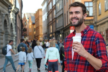 Gorgeous male holding a disposable cup of coffee in the a crowded city street