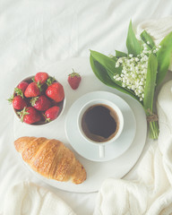 breakfast in bed. croissant, cup of coffee and  Lily of the valley