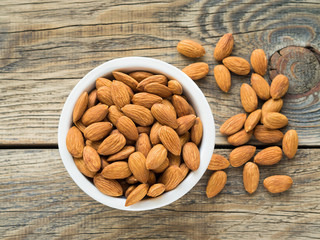 Top view of white cups, bowls with a handful of pecans, almonds on a wooden background