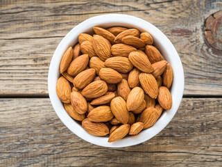 Top view of white cups, bowls with a handful of pecans, almonds on a wooden background