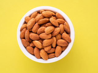 Top view of white cups, bowls with a handful of pecans, almonds on a bright yellow background color