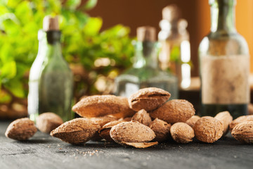 Heap of almond in shell on a black wooden table and vintage glass bottles with greenery in the background