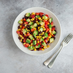 Avocado, black  bean, corn and bell pepper salad in white bowl