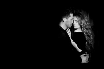 Beautiful couple in love hugging against black background. Studio black and white portrait photo of...