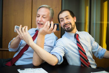 Two smiling colleagues showing their phones to each other