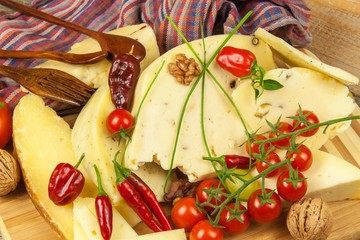 Sliced hard cheese on the kitchen board. Production of cheeses on the farm. Spicy cheese, tomatoes, garlic, chilli, pepper.