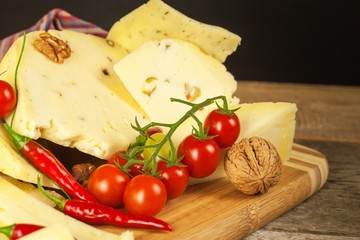 Sliced hard cheese on the kitchen board. Production of cheeses on the farm. Spicy cheese, tomatoes, garlic, chilli, pepper.