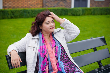 Mature simple woman of plus size, American or European appearance walks in the city enjoying life. Cute lady with excess weight, dressed in jacket and scarf going around old part of town