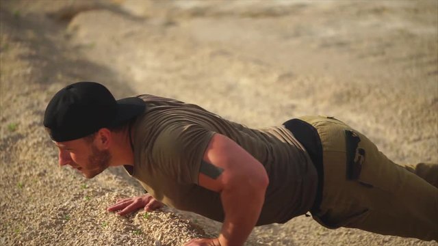 Muscular young man working out outdoor at sunset. He doing push-ups on graveled ground
