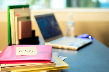 Wealth; Stack of Documents and Laptop at working Desk.