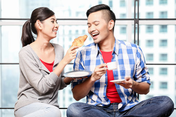 Young asian couple, woman and man, having breakfast together in skyscraper apartment