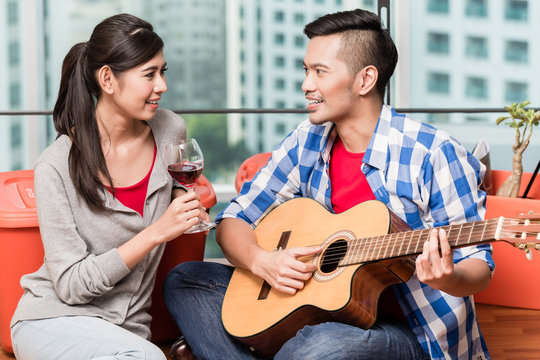 After moving together in city apartment young man plays love song for his girlfriend on guitar