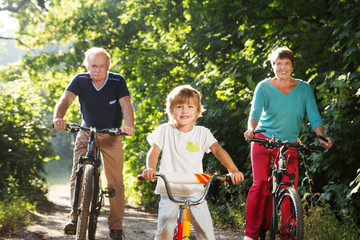 happy family the grandmother, the grandfather and the grandson ride a bike outdoors