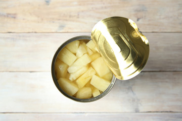 Opened tin can of canned pineapple pieces. Canned pineapple in can on wooden table top view.