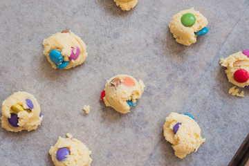 Scoops of cookie dough with colorful chocolate candies on baking sheet