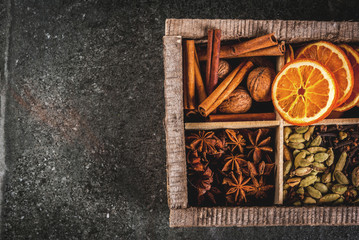 Christmas spices for baking, cocktails, mulled wine, with gingerbread cookies (stars) - dried apple, orange, cardamom, cloves, cinnamon, anise.  old wooden box, black stone table. copy space top view