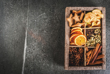 Christmas spices for baking, cocktails, mulled wine, with gingerbread cookies (stars) - dried apple, orange, cardamom, cloves, cinnamon, anise.  old wooden box, black stone table. copy space top view