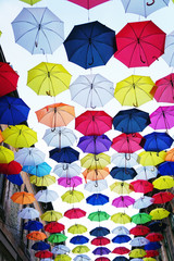 Fototapeta na wymiar Colorful umbrellas background. Coloruful umbrellas urban street decoration. Hanging Multicoloured umbrellas over blue sky.