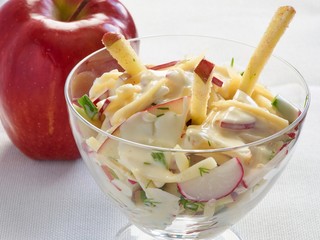 Fresh vegetarian salad with radish and apple in a glass bowl on white tablecloth with apple in corner
