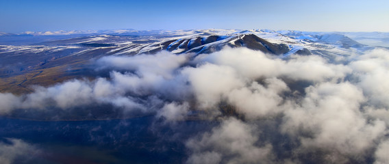 Obraz premium Aerial view mountain landscape in Siberia with peaks covered by snow and clouds.