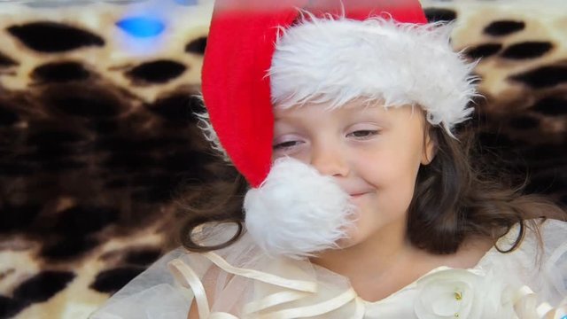 Happy child in a Christmas hat. Beautiful little girl is playing with santa claus cap.