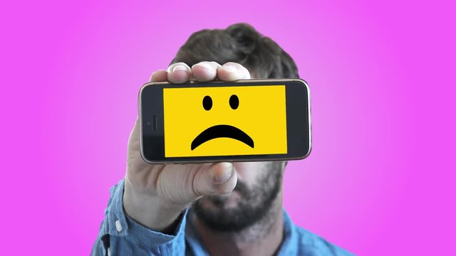 Sad Man With Smiley Face On Smartphone. Man shows his feelings through a smartphone with a sad Smiley face on screen